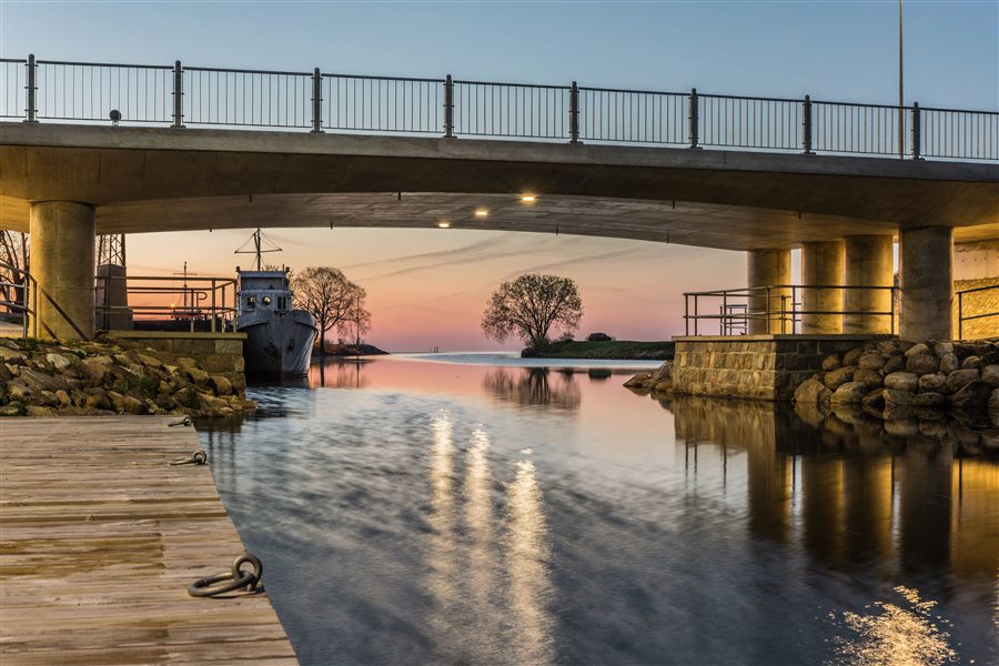 Päikesetõus Mustvee sadamas — laev silla all kai ääres, taevas roosa ja kuldne.